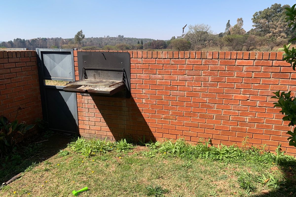 A rear garden area featuring a brick boundary wall, a built-in braai, and a metal access gate.