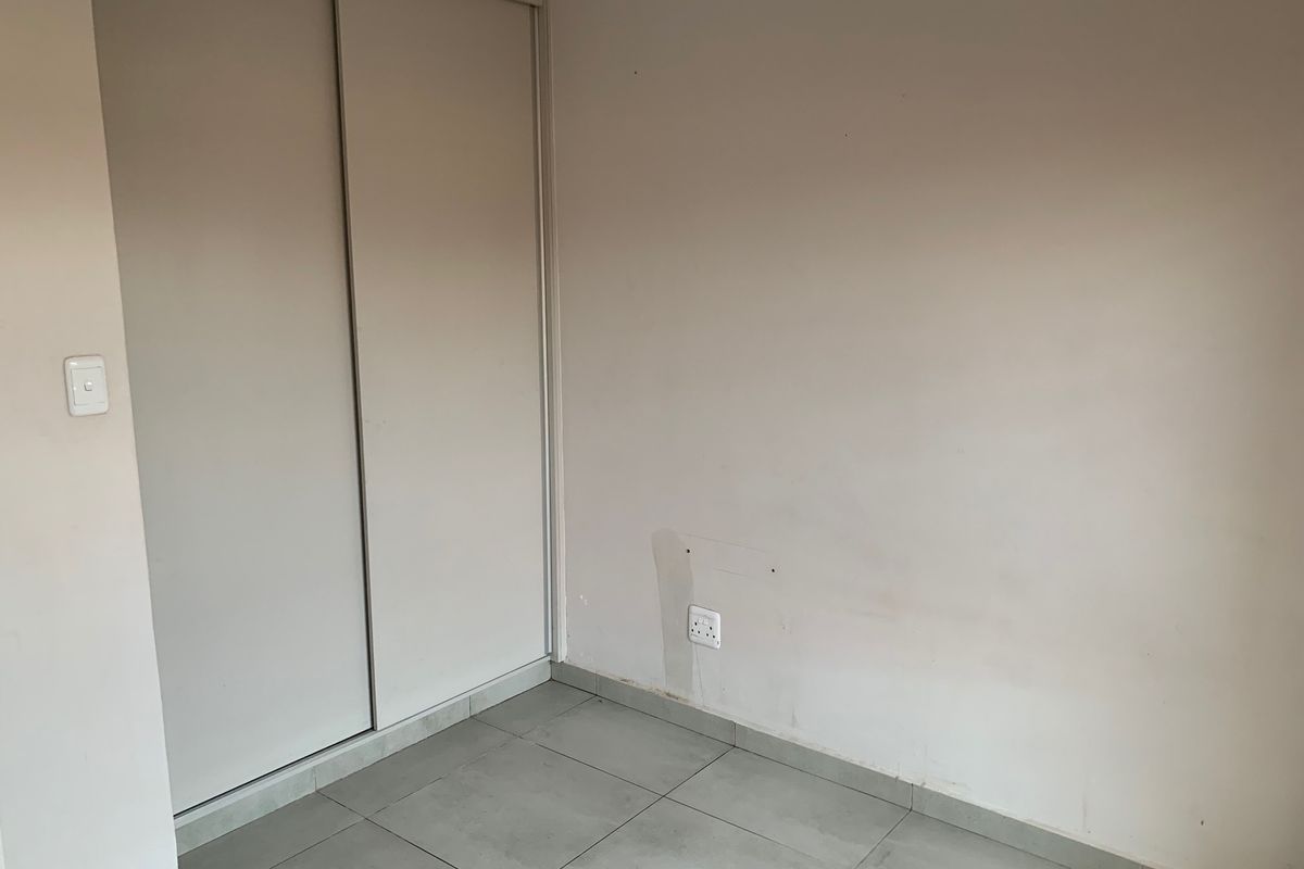 An empty bedroom featuring tiled flooring and a built-in sliding door wardrobe, ready for personalization.