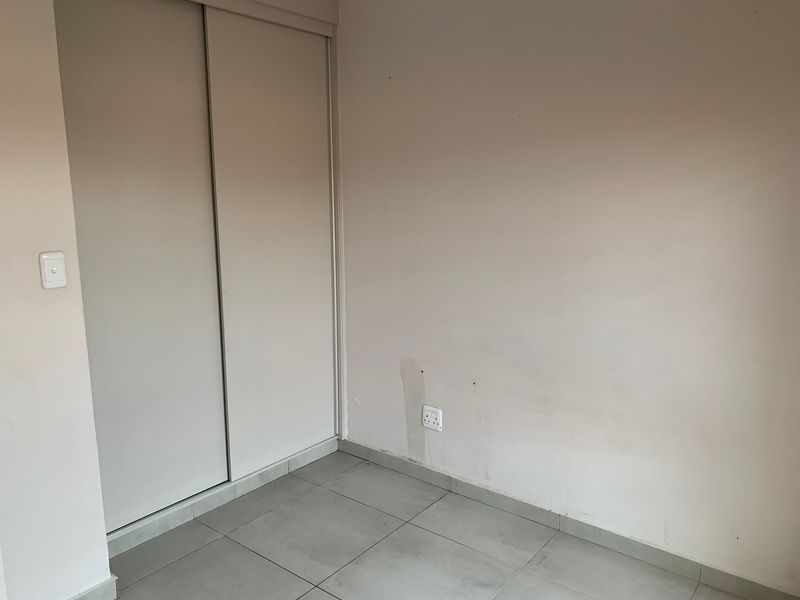 An empty bedroom featuring tiled flooring and a built-in sliding door wardrobe, ready for personalization.