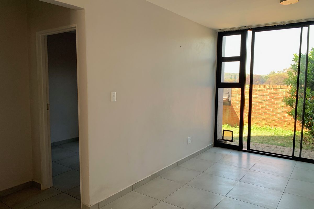 An empty living room featuring neutral tiled flooring and a large sliding glass door providing access to the outdoor area.