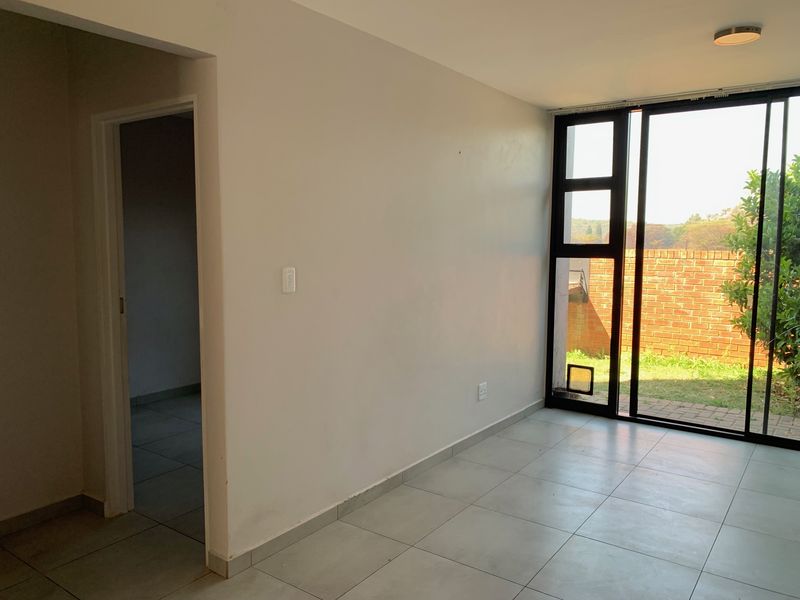 An empty living room featuring neutral tiled flooring and a large sliding glass door providing access to the outdoor area.
