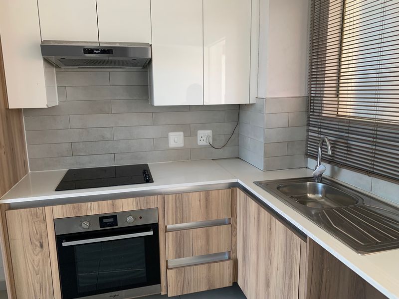 Modern kitchen featuring wood-look cabinetry, white upper cabinets, a built-in electric oven and hob, and a stainless steel sink with a tiled backsplash.