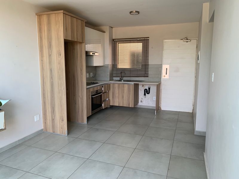 A compact kitchen featuring wood-look cabinetry, built-in oven and hob, and tiled flooring. The space requires minor repairs to the under-sink area.