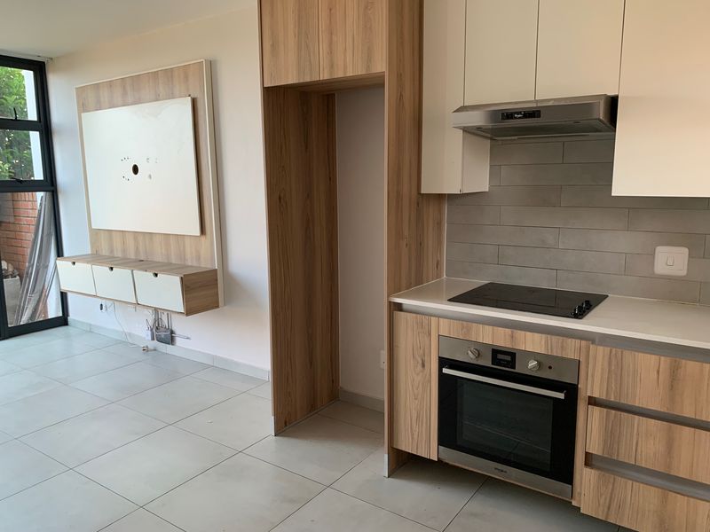 Modern open-plan living area featuring a contemporary kitchen with built-in appliances, sleek cabinetry, and a matching wall-mounted media unit.