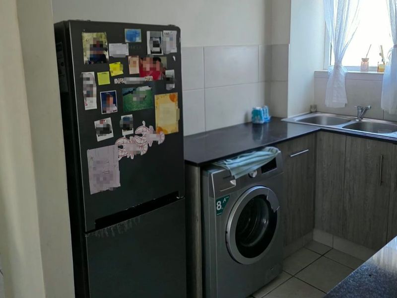 A functional kitchen area featuring laminate cabinetry, stone countertops, a double sink, and tiled flooring with a dedicated space for laundry appliances.