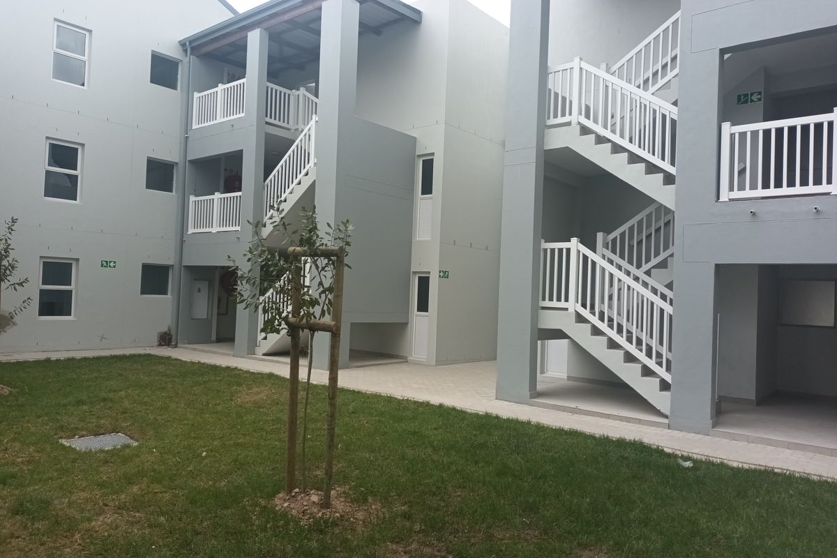 A view of the townhouse complex exterior featuring multi-level staircases, white railings, paved walkways, and a communal lawn area.