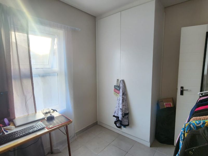 A functional bedroom featuring neutral tiled flooring, a built-in white wardrobe, and a window providing natural light.