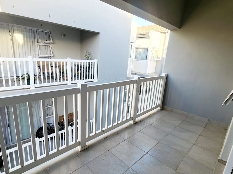 A clean, covered balcony featuring tiled flooring and a white balustrade railing, offering an open outdoor space connected to the main living area.