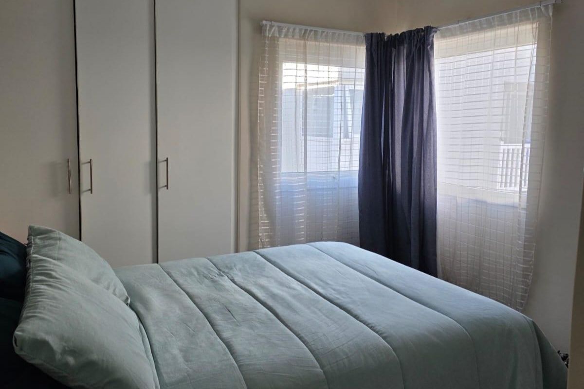 A functional bedroom featuring built-in cupboards and natural light through corner windows.