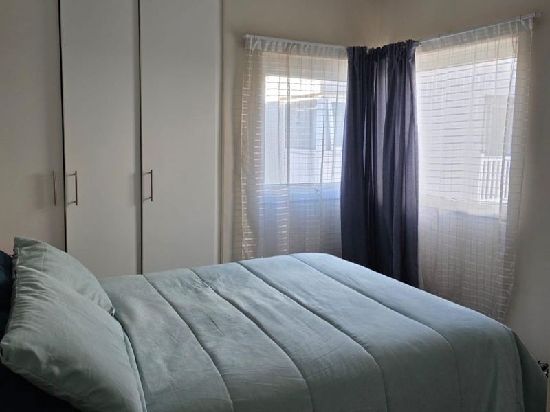 A functional bedroom featuring built-in cupboards and natural light through corner windows.
