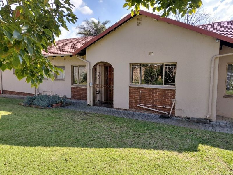 A view of the rear exterior of the house featuring a tiled roof, brick and plaster facade, security gate, and a paved walkway leading to the entrance.