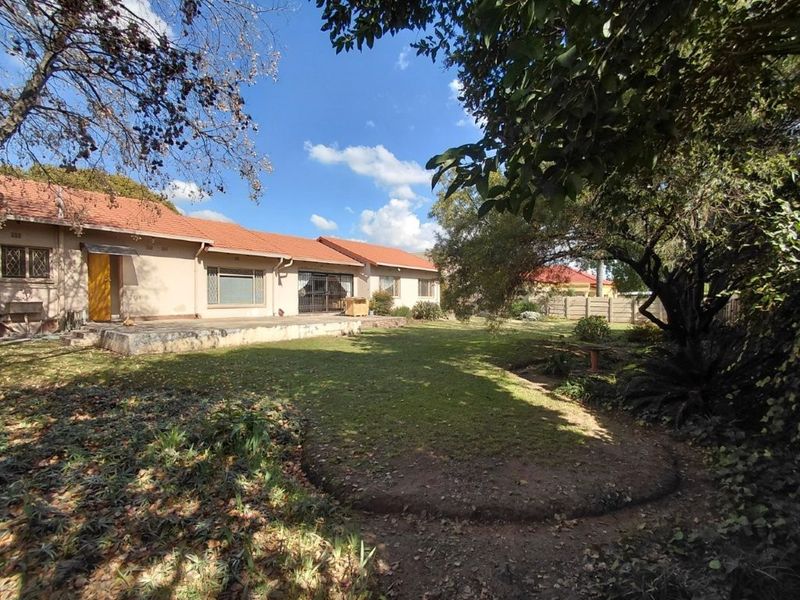 Rear view of the property featuring a tiled roof, a concrete patio area, and a spacious garden enclosed by precast walling.