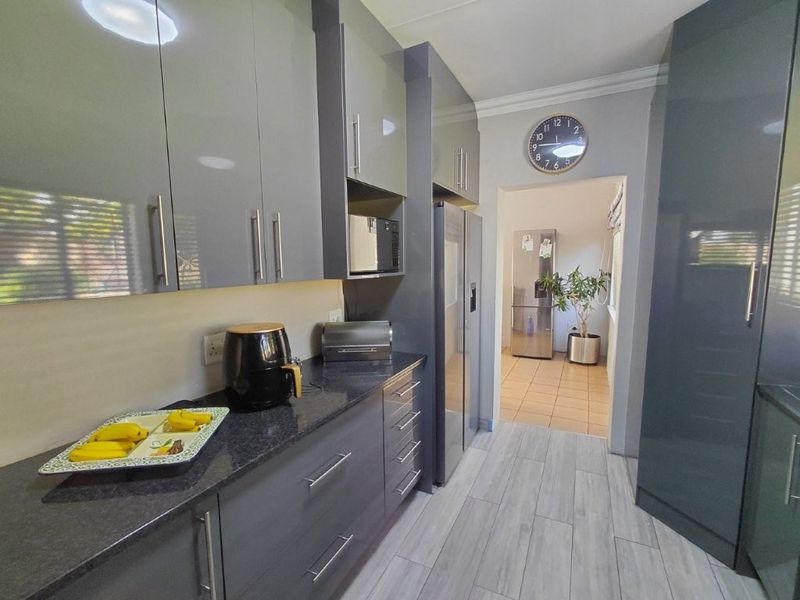 Modern kitchen featuring sleek grey cabinetry, granite countertops, and integrated appliances, leading into a secondary utility or pantry area.