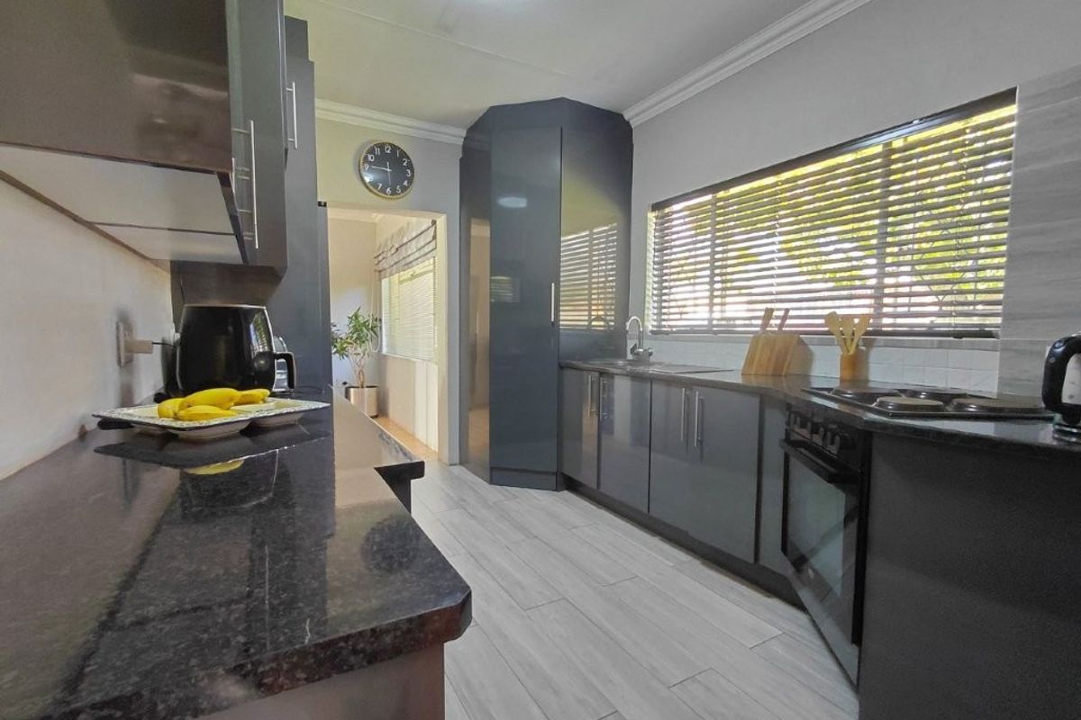 Modern kitchen featuring dark grey cabinetry, granite countertops, built-in oven and hob, and light-toned tiled flooring with ample natural light.