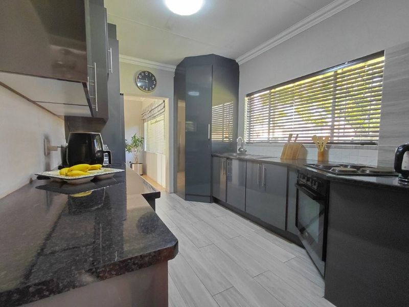 Modern kitchen featuring dark grey cabinetry, granite countertops, built-in oven and hob, and light-toned tiled flooring with ample natural light.