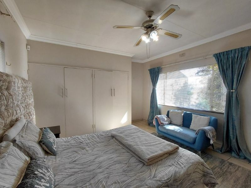 Spacious bedroom featuring built-in cupboards, a ceiling fan, and large windows with venetian blinds, offering a comfortable and functional living space.