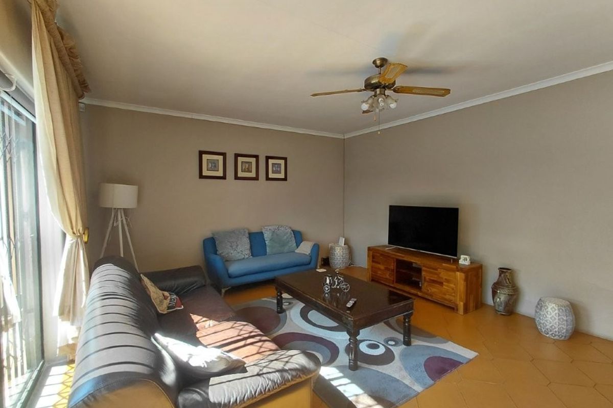 A comfortable living room featuring tiled flooring, a ceiling fan, and large sliding glass doors providing natural light.