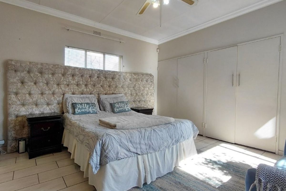 Spacious bedroom featuring tiled flooring, built-in cupboards, and a ceiling fan, offering a functional layout with neutral finishes.