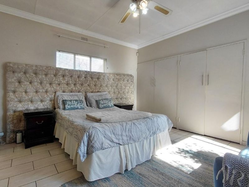 Spacious bedroom featuring tiled flooring, built-in cupboards, and a ceiling fan, offering a functional layout with neutral finishes.