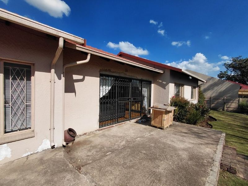 Rear exterior view of the house featuring a concrete patio area, security gates, and visible exterior wall maintenance requirements.