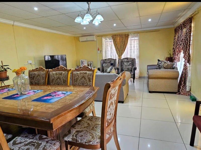 Spacious open-plan living and dining area featuring tiled flooring, a drop ceiling with integrated lighting, and a wall-mounted air conditioning unit.