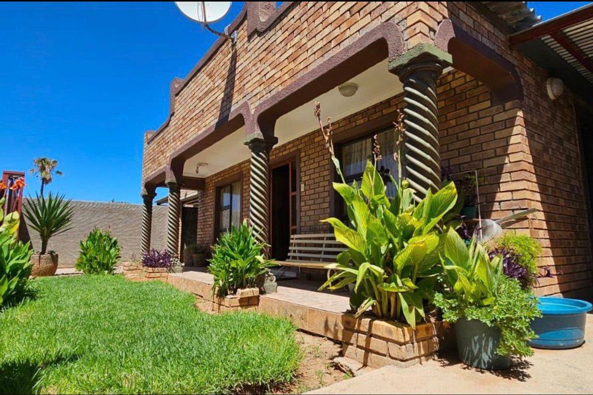 A rear exterior view of a face brick house featuring a covered patio with decorative columns and a small garden area.