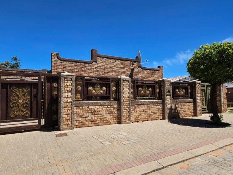 Front view of the property featuring a secure brick boundary wall with decorative metal gates and a paved driveway.