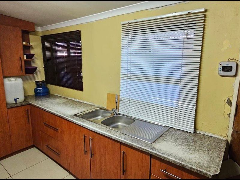 A functional kitchen featuring wood-look cabinetry, a stainless steel double sink, and tiled flooring, currently requiring cosmetic wall repairs and updates.