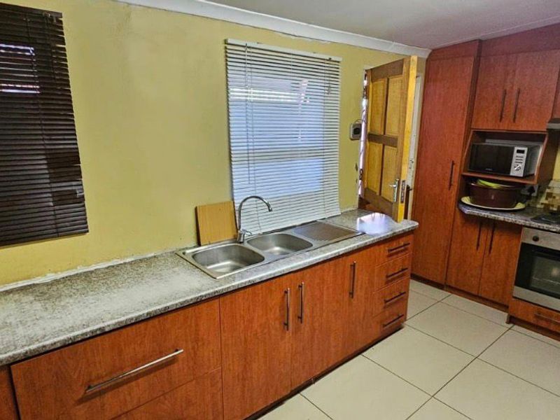 A functional kitchen featuring wood-finish cabinetry, laminate countertops, a double sink, and integrated appliances including an oven and hob with a mosaic backsplash.