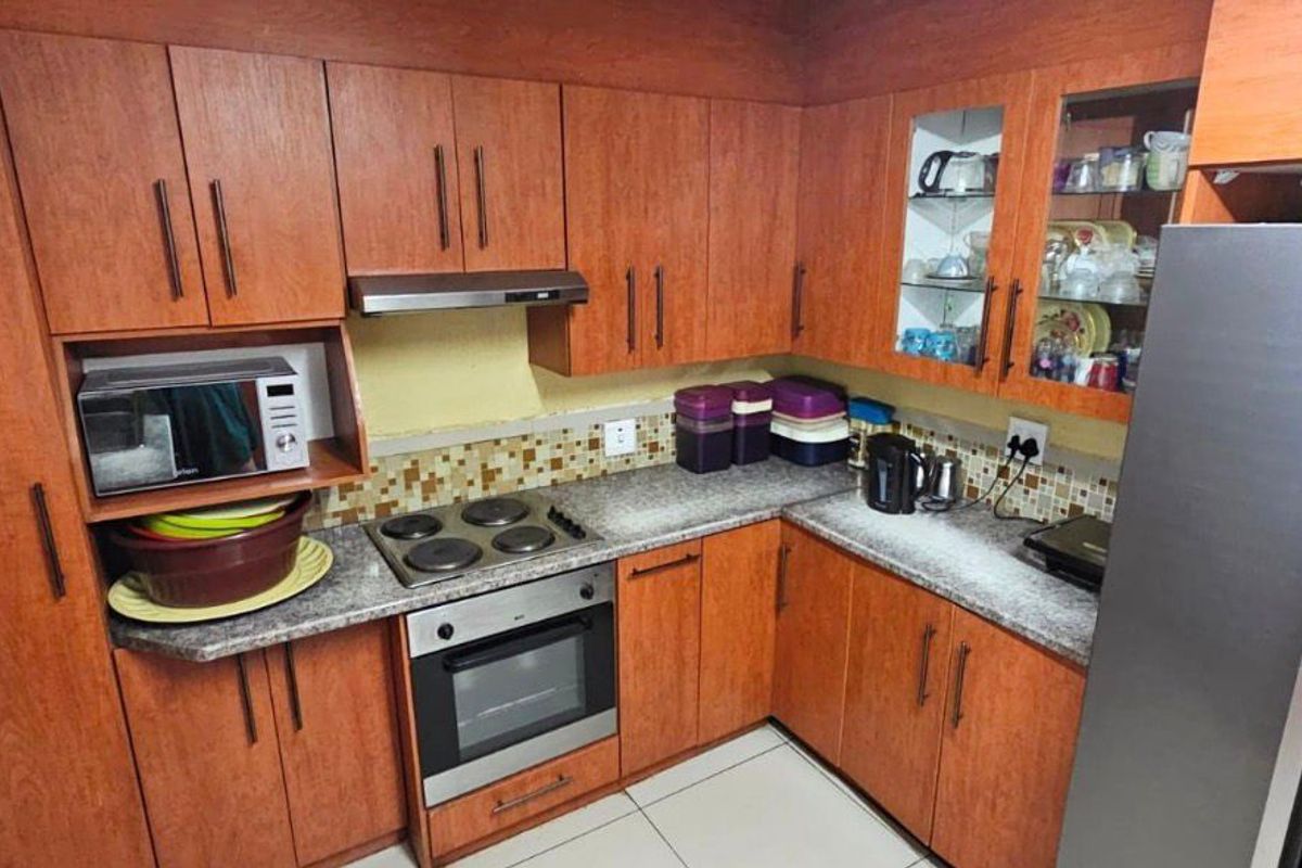 A functional kitchen featuring wood-finish cabinetry, granite-look laminate countertops, a mosaic tile backsplash, and integrated appliances including an oven and hob.