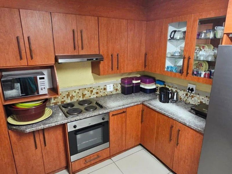 A functional kitchen featuring wood-finish cabinetry, granite-look laminate countertops, a mosaic tile backsplash, and integrated appliances including an oven and hob.