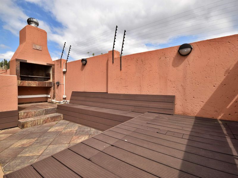Outdoor patio area featuring a built-in braai, timber decking, and perimeter wall with electric fencing.