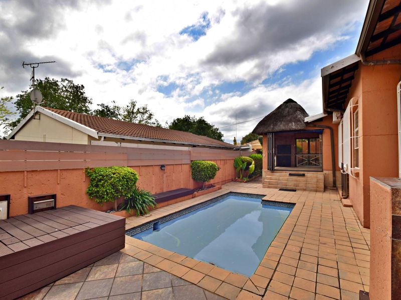 Outdoor pool area featuring a paved patio, timber decking, and a thatched lapa, providing a functional space for outdoor entertainment.
