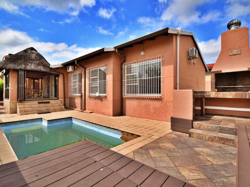 Rear exterior view featuring a swimming pool, tiled patio area, and a built-in outdoor braai facility.