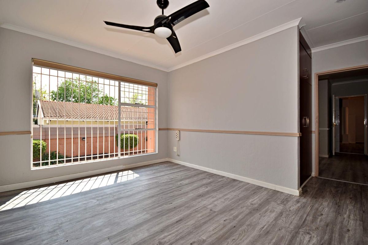 A bright, empty bedroom featuring modern laminate flooring, a ceiling fan, and built-in cupboards, offering a clean and neutral space ready for personalization.