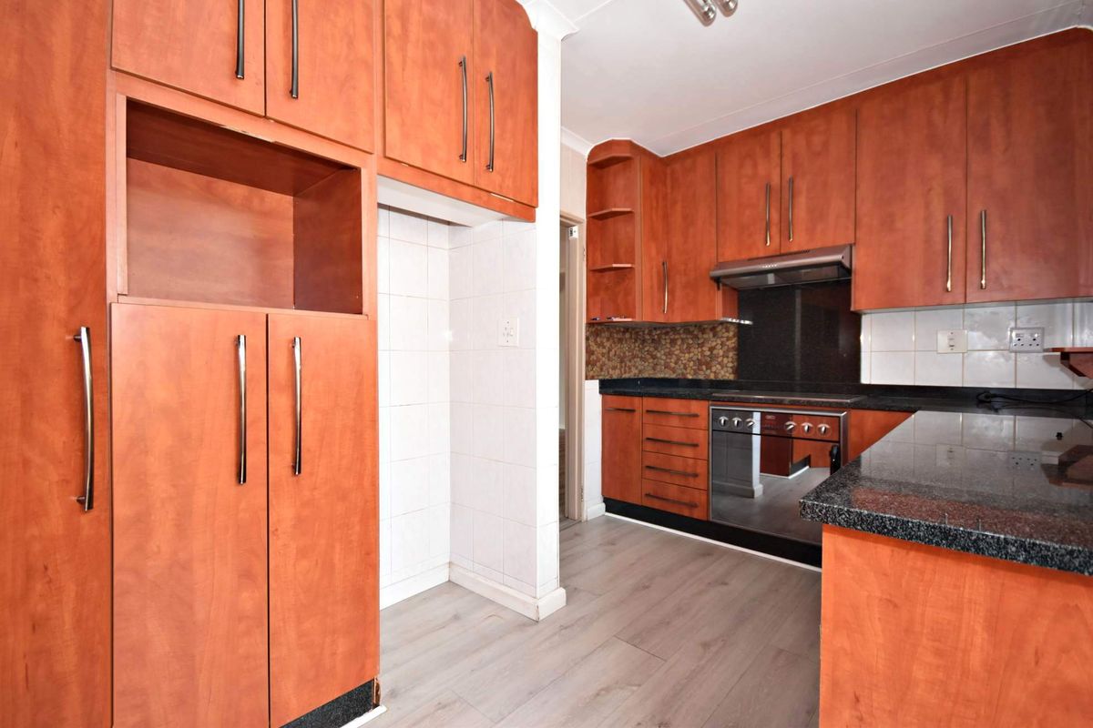 A functional kitchen featuring warm-toned built-in cabinetry, granite countertops, a built-in oven with extractor fan, and light-colored laminate flooring.