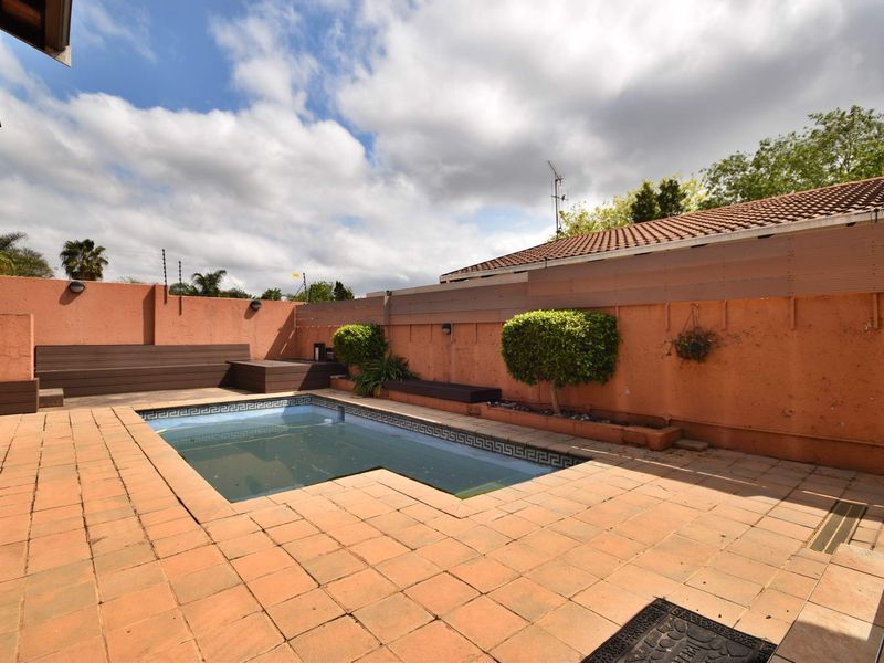 Outdoor pool area featuring a tiled deck, built-in timber bench seating, and perimeter boundary walls with raised planter beds.