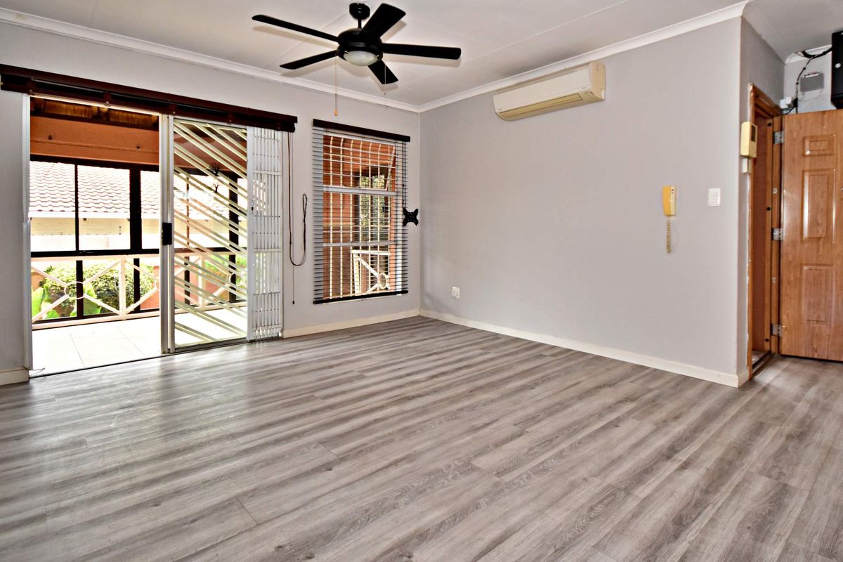 Spacious living area featuring modern laminate flooring, a ceiling fan, split-system air conditioning, and direct access to a covered patio through sliding glass doors.