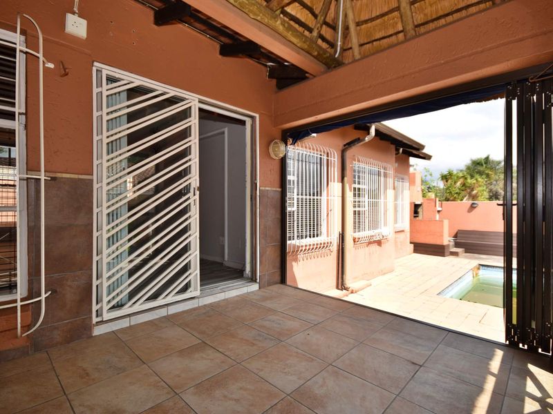 A covered patio area featuring a thatched roof, tiled flooring, and security gates, providing direct access to the outdoor pool area.