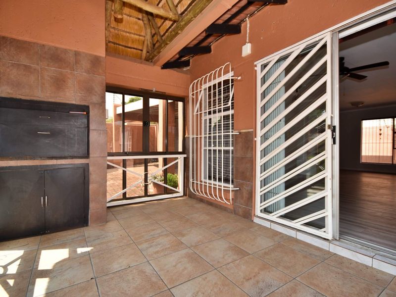 Covered patio area featuring a built-in braai, tiled flooring, and a thatch roof, providing a functional outdoor entertainment space.