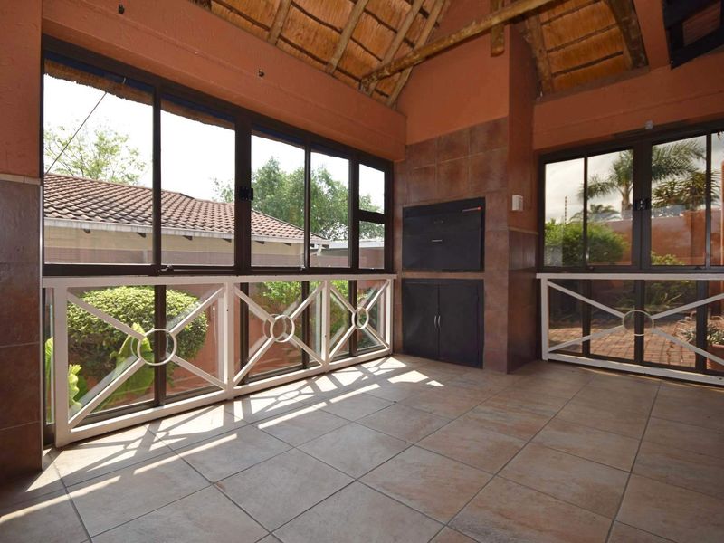 A covered patio area featuring a thatched roof, tiled flooring, and a built-in braai, offering a versatile outdoor entertainment space.