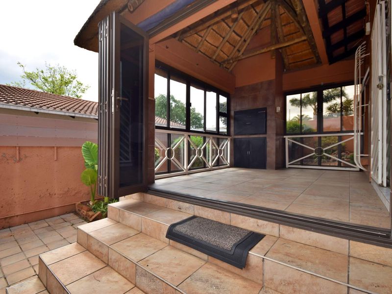 Covered patio area featuring a thatched roof, tiled flooring, and a built-in braai, providing a functional outdoor entertainment space.