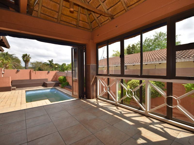 Covered patio area featuring a thatched roof, tiled flooring, and bi-fold doors opening directly onto a private swimming pool and garden space.