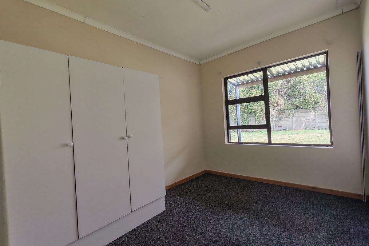 An empty bedroom featuring built-in cupboards, carpet flooring, and a large window overlooking the rear garden.
