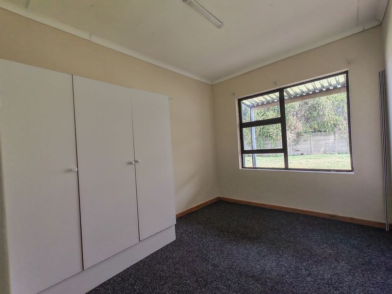 An empty bedroom featuring built-in cupboards, carpet flooring, and a large window overlooking the rear garden.