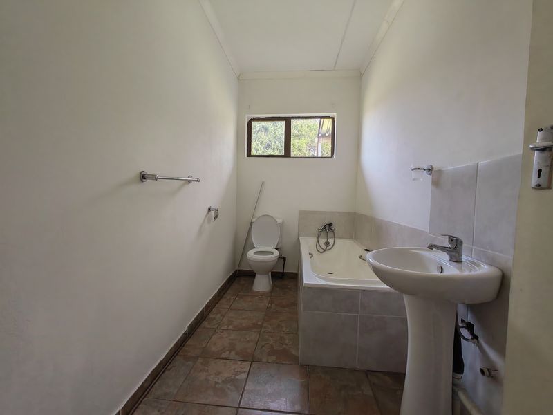 A functional bathroom featuring a pedestal basin, built-in bathtub, and toilet with tiled flooring, offering a blank canvas for renovation.