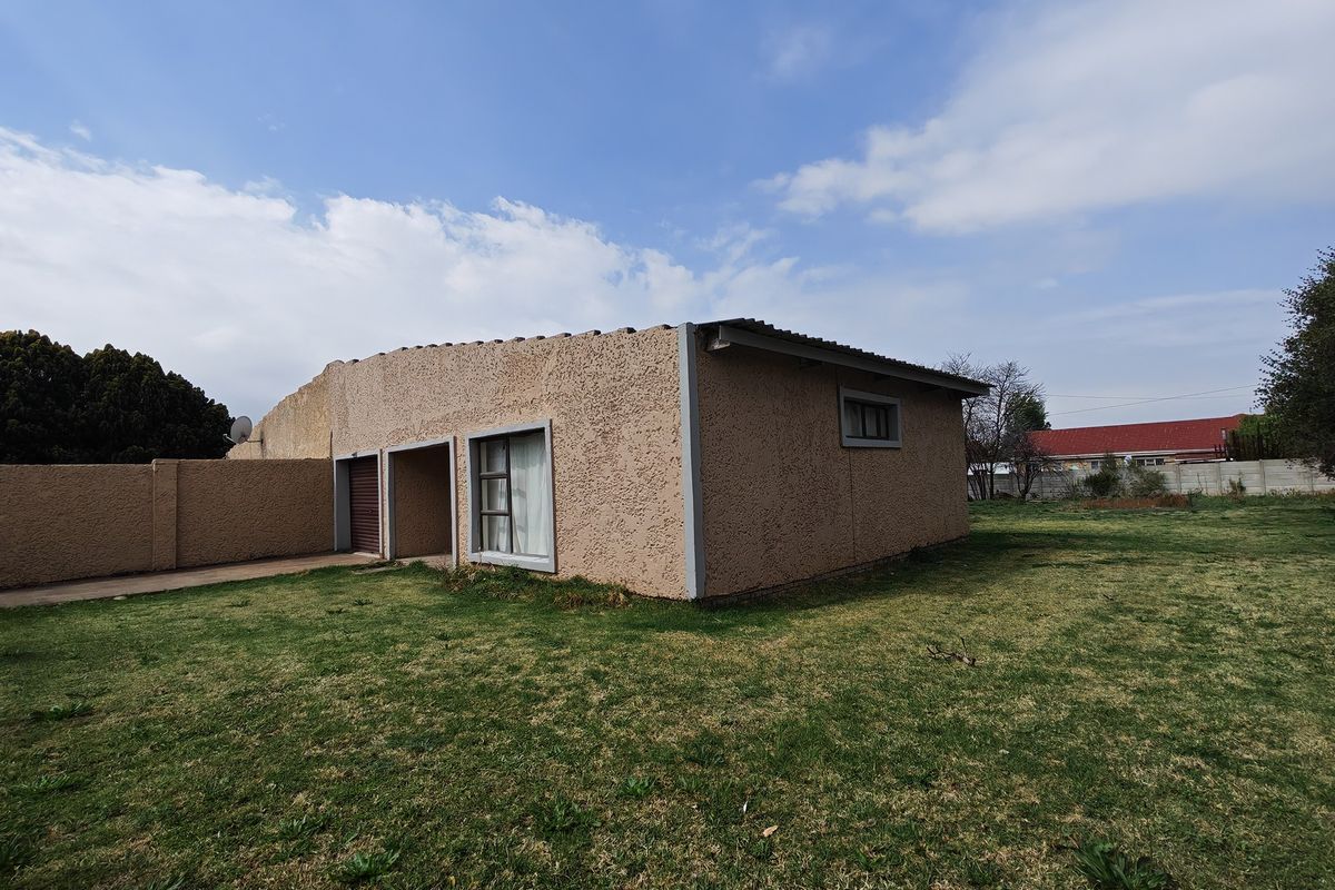 Rear view of the property featuring a textured stucco facade, tiled roof, and a spacious backyard with boundary walling.