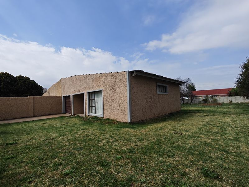 Rear view of the property featuring a textured stucco facade, tiled roof, and a spacious backyard with boundary walling.