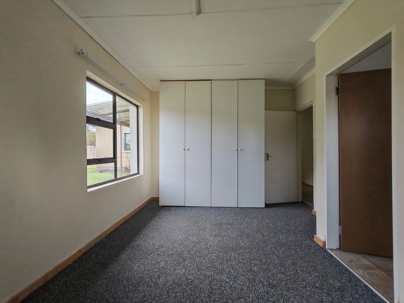 An empty bedroom featuring built-in cupboards, carpeted flooring, and a large window providing natural light.