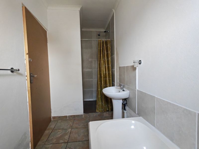 A functional bathroom featuring a pedestal basin, shower enclosure, and tiled finishes, currently requiring some cosmetic maintenance and updates.